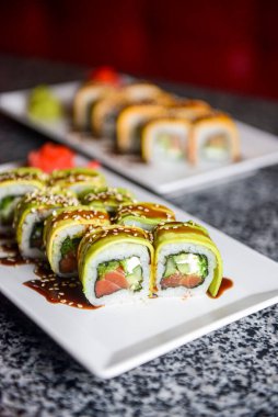 Philadelphia ya da California avokado ve krem peynirli suşi sarar. Yeşil ejderha suşisi. Geleneksel Japon yemeği konsepti. Restoranda beyaz bir tabakta servis edilir, konsepti dışarıda yenir..