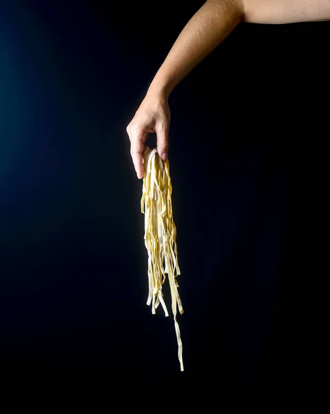 Hand throwing egg noodles on dark background, Flying cooked pasta in hands over black. Creative advertisement, advert concept for Italian macaroni pasta noodles.