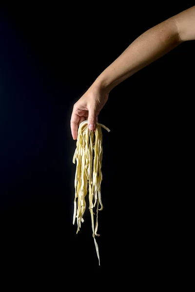 暗い背景に卵麺を投げる手 黒の上に手で調理されたパスタを飛んで 創造的な広告 イタリアのマカロニパスタ麺の広告コンセプト ロイヤリティフリーのストック写真