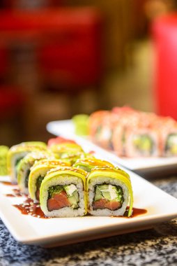 Philadelphia ya da California avokado ve krem peynirli suşi sarar. Yeşil ejderha suşisi. Geleneksel Japon yemeği konsepti. Restoranda beyaz bir tabakta servis edilir, konsepti dışarıda yenir..