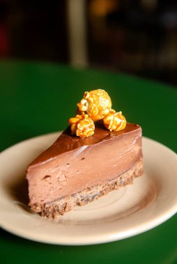 Çikolatalı cheesecake dilimi, üzerinde karamelli patlamış mısır olan beyaz tabakta, bir restoranda ya da kafede. Tatlı zamanı, bir parça çikolatalı pasta..