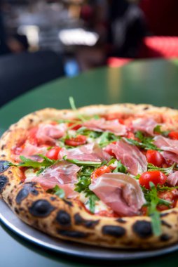 Jambonlu, domatesli ve mantarlı pizza bir restoranın içindeki masada yuvarlak bir tepside servis edilir. Geleneksel İtalyan pizza tarifi.