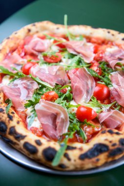 Jambonlu, domatesli ve mantarlı pizza bir restoranın içindeki masada yuvarlak bir tepside servis edilir. Geleneksel İtalyan pizza tarifi.