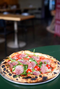 Jambonlu, domatesli ve mantarlı pizza bir restoranın içindeki masada yuvarlak bir tepside servis edilir. Geleneksel İtalyan pizza tarifi.