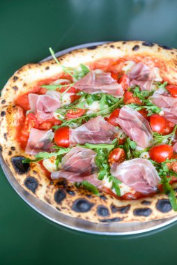 Jambonlu, domatesli ve mantarlı pizza bir restoranın içindeki masada yuvarlak bir tepside servis edilir. Geleneksel İtalyan pizza tarifi.