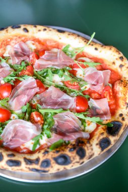 Jambonlu, domatesli ve mantarlı pizza bir restoranın içindeki masada yuvarlak bir tepside servis edilir. Geleneksel İtalyan pizza tarifi.