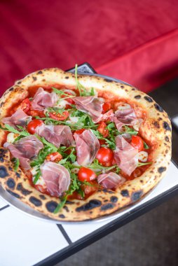 Jambonlu, domatesli ve mantarlı pizza bir restoranın içindeki masada yuvarlak bir tepside servis edilir. Geleneksel İtalyan pizza tarifi.