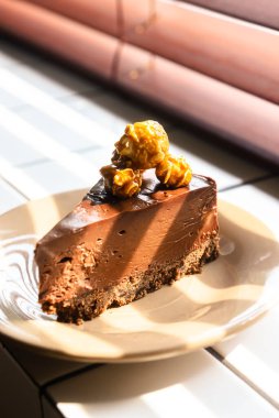 Çikolatalı cheesecake dilimi, üzerinde karamelli patlamış mısır olan beyaz tabakta, bir restoranda ya da kafede. Tatlı zamanı, bir parça çikolatalı pasta..