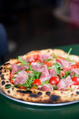 Jambonlu, domatesli ve mantarlı pizza bir restoranın içindeki masada yuvarlak bir tepside servis edilir. Geleneksel İtalyan pizza tarifi.