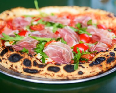 Jambonlu, domatesli ve mantarlı pizza bir restoranın içindeki masada yuvarlak bir tepside servis edilir. Geleneksel İtalyan pizza tarifi.