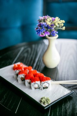 Krem peynirli suşi ve tepesinde kırmızı havyar. Restorandaki siyah ahşap masada beyaz bir tabakta servis ediliyor. Japon mutfağı kavramı.