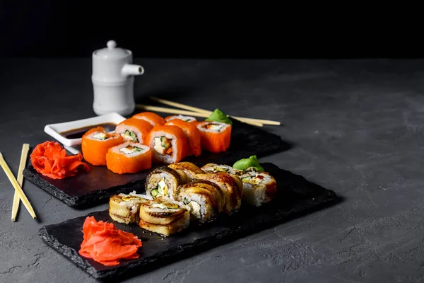 Set of Philadelphia or California sushi and set of Eel sushi on black stone slate. Over grey, over gray background. Japanese cuisine concept. Creative adverticement concept, vertical banner.