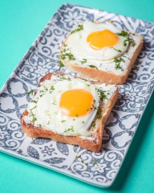 Geleneksel kahvaltı kavramı - yumurtalı ekmek ve taze yeşillik. Mavi ya da turkuaz arka planda renkli bir tabakta servis edilir.