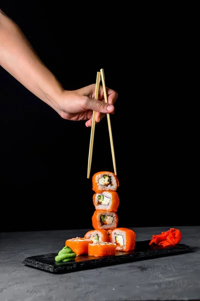 黒い石のスレートでフィラデルフィアやカリフォルニアの寿司のセット 灰色の背景の上に 日本料理のコンセプト クリエイティブ広告コンセプト 垂直バナー 箸で寿司を食べる ロイヤリティフリーのストック画像