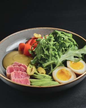 Haşlanmış yumurta, avokado, taze domates ve siyah arka planda roka kaplı somon balığı. Sağlıklı beslenme konsepti, Japon mutfağı.