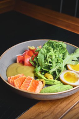Haşlanmış yumurta, avokado, taze domates ve siyah arka planda roka kaplı somon balığı. Sağlıklı beslenme konsepti, Japon mutfağı.