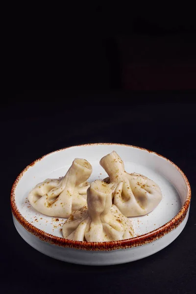 Khinkali cooked on a ceramic plate over black background. Traditional Georgian cuisine concept, three khinkali on white ceramic plate. Vertical banner.