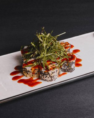 Suşi rulolarını siyah arka planda beyaz tepsiye koy. Japon mutfağı konsepti, Nori üstte..