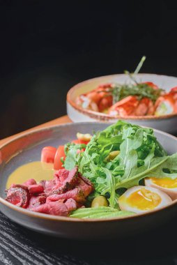 Kaynamış yumurtalı Carpaccio eti, avokado, taze domates ve siyah arka plan masasının üzerinde bir tabakta roka. Sağlıklı yeme kavramı