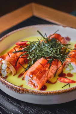 Siyah bir masada servis edilen krem peynirli füme somon ruloları ve bulanık bir arka plan. Japon mutfağı uygun..