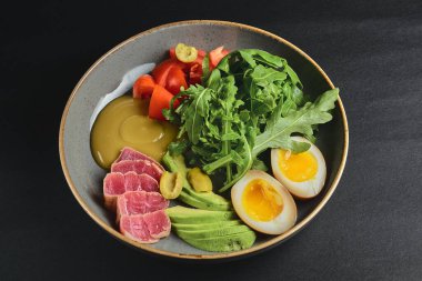 Haşlanmış yumurta, avokado, taze domates ve siyah arka planda roka kaplı somon balığı. Sağlıklı beslenme konsepti, Japon mutfağı.