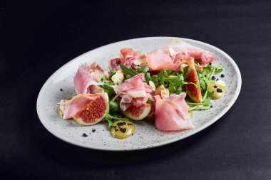 Siyah arkaplanlı beyaz tabakta servis edilen taze incirli jambon salatası. Sağlıklı yeme kavramı.
