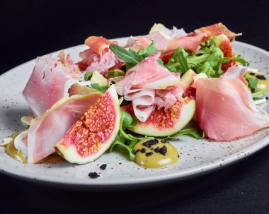Siyah arkaplanlı beyaz tabakta servis edilen taze incirli jambon salatası. Sağlıklı yeme kavramı.