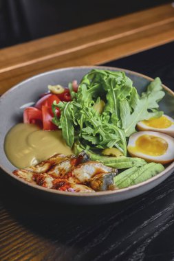 Yılanbalıklı Sashimi Suşi, haşlanmış yumurta, avokado, taze domates ve siyah arka planda bir tabakta roka. Sağlıklı beslenme konsepti, Japon mutfağı.