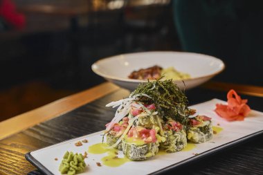 Somon, avokado ve nori soslu sıcak suşi. Lezzetli, iştah açıcı ve tuzlu suşi seti beyaz tabakta servis ediliyor. Japon mutfağı konsepti. Yan görünüm.