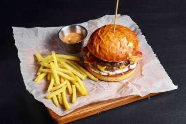Siyah arka planda taze lezzetli bir burger, yanında sos ve patates kızartması. Fast food, abur cubur konsepti. Siyahtan önce lezzetli sulu burger. Yeni menü.
