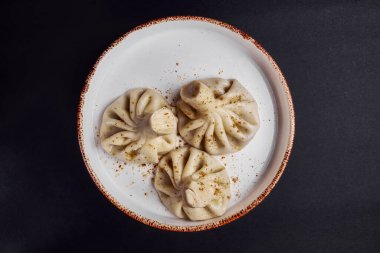 Khinkali siyah arka planda seramik bir tabakta pişirildi. Geleneksel Gürcistan mutfağı konsepti, beyaz seramik tabakta üç hinkali. Dikey pankart.