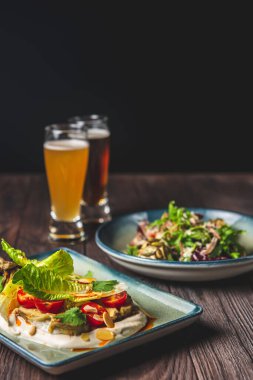 İki tabak sağlıklı sonbahar ya da mantarlı sonbahar salatası, vişneli domates, krema sosu. Kırsal ahşap masa zemininde iki bardak birayla servis edilir..