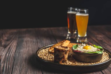 Köy ahşap masa üzerinde siyah arka planda iki bardak birayla sığır etli tartar servis edilir. Geleneksel tarif.