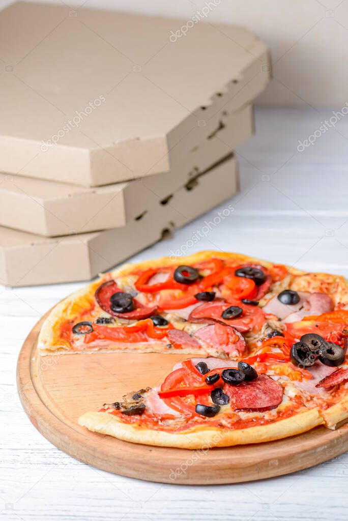 Sliced whole salami pepperoni pizza on a wooden table. Traditional pepperoni pizza recipe, Italian cuisine concept. Fast food, junk food. Delivery boxes near pizza, delivery or takeout concept.