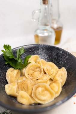 Geleneksel haşlanmış hamur köfteleri siyah bir kasede taze otlar ve baharatlarla fotokopi alanı olan hafif bir arka planda..