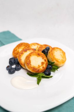 Beyaz tabakta servis edilen yaban mersinli ve taze naneli süzme peynirli krep. Hafif ışıklandırmalı en az gıda fotoğrafçılığı.