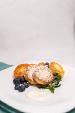 Yaban mersinli, naneli, ekşi kremalı, beyaz tabakta çatal bıçaklı ve yeşil tekstil arka planlı peynirli krep..