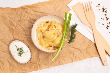 Geleneksel Ukrayna Varenyky 'sinin en iyi manzarası kızarmış soğan, ekşi krema ve parşömen kağıdında taze otlarla servis edilir. Düz konumda yemek fotoğrafçılığı.