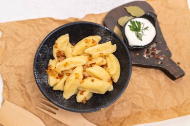 Geleneksel Ukrayna palushky patates köfteleri kızarmış soğanlı siyah seramik bir kasede servis edilir. Ekşi krema soslu ve otlu kırsal yemek tasarımı..