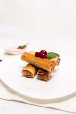 Kiraz dolgulu, kiraz ve nane yaprağıyla kaplı altın rulo krepler. Temiz ve en az tatlı bileşimi.