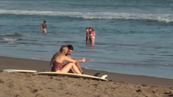 女孩坐在岸边的沙滩上的家伙 — 图库视频影像