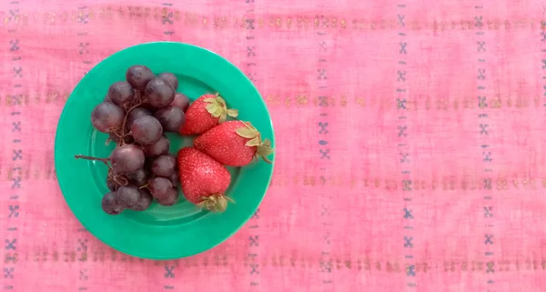 Vue du dessus des raisins avec des fraises dans une assiette — Photo