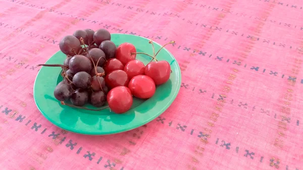 Cerejas e uvas em uma placa — Fotografia de Stock