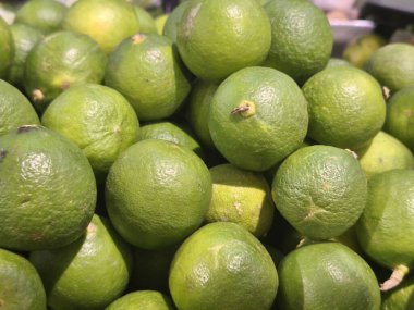 Canlı renklerini ve dokularını sergileyen taze yeşil limon yığınının yakın plan çekimi, muhtemelen bir pazarda..