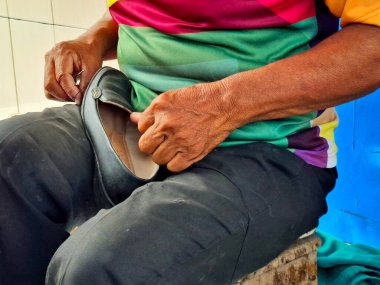 Bir zanaatkarın eli dikiş dikerek bir kadının ayakkabısının tabanını onarıyor. Sokaktaki küçük işletmeler.
