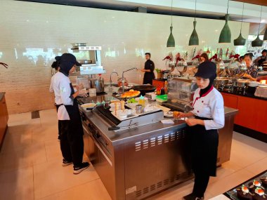 Magelang - Endonezya, 31 Aralık 2025. Bir otel restoranında servis masası, kahvaltı sırasında otel misafirleri. Çeşitli Batı, geleneksel, yerel ve Doğu Asya yemeklerinin yanı sıra çeşitli ekmekler, kekler, meyveler sunuluyor..