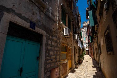 Rovinj, Hırvatistan - 14 Ağustos 2025: Güneşli taş duvarları, renkli kapıları ve yeşil kepenkleri olan dar kaldırım taşı sokak, eski kasaba yaşamının dokusunu ve sessiz ritmini yansıtıyor.