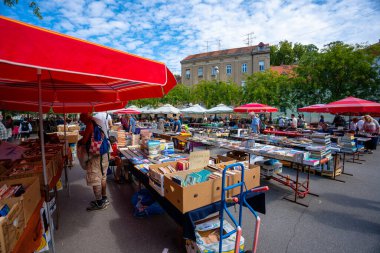 Zagreb, Hırvatistan - 23 Ağustos 2024: Zagreb 'deki güneşli sabah bit pazarı, kırmızı şemsiyeler altında tezgahlar, antika, giysi ve ilginç eşyalar satan satıcılar.