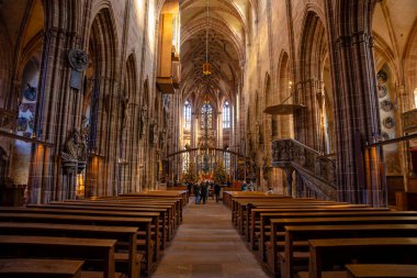 Nurnberg, Almanya - 26 Aralık 2024: Yüksek kemerler, süslü taş oymalar, vitray pencereler ve sıcak güneş ışığıyla aydınlatılan ahşap sıraların yer aldığı büyük gotik bir katedralin içi