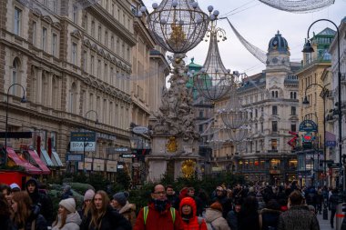 Viyana, Avusturya: 19 Aralık 2024: Parlak avizeler, dekore edilmiş anıtlar ve tarihi binalar arasında şenlikli kalabalıklarla dolu canlı bir Noel sokak sahnesi.